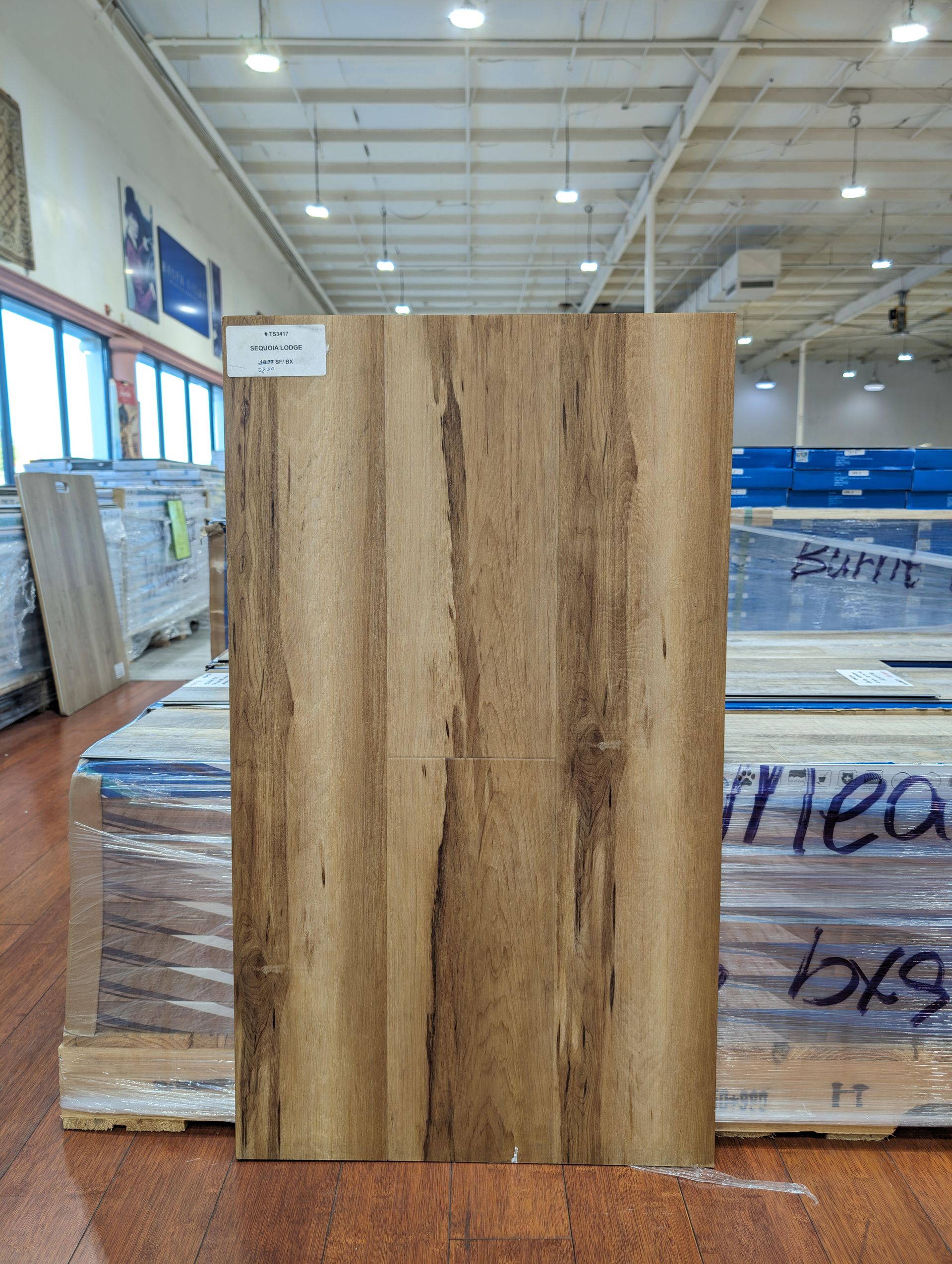 A wooden plank sample with vertical grain pattern, in a warehouse setting.