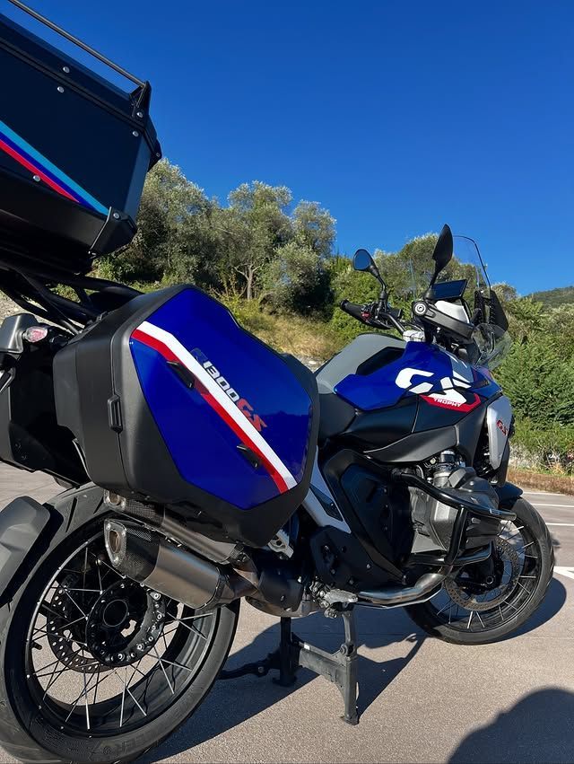Motocicletta BMW blu parcheggiata sul ciglio di una strada soleggiata, con valigie laterali nere e uno sfondo collinare.