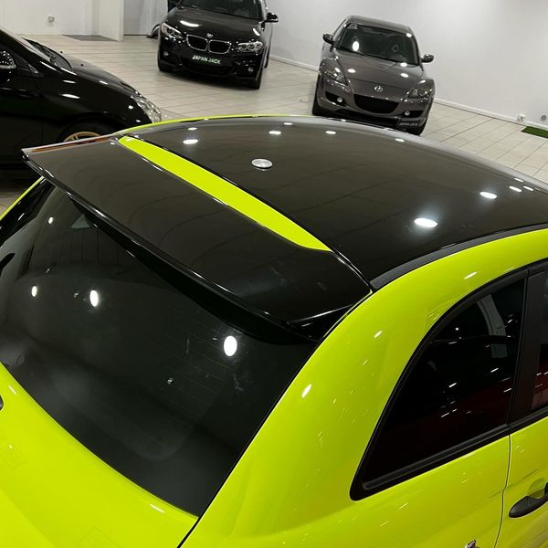 Auto di un verde lime brillante con tetto nero in uno showroom al coperto, vista dall'alto.