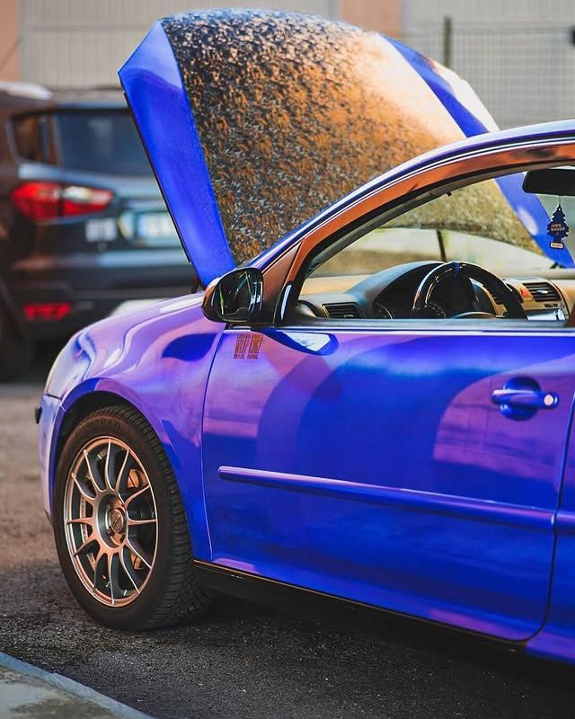 Auto sportiva blu con cofano aperto in un parcheggio, vista laterale con cerchi in bronzo