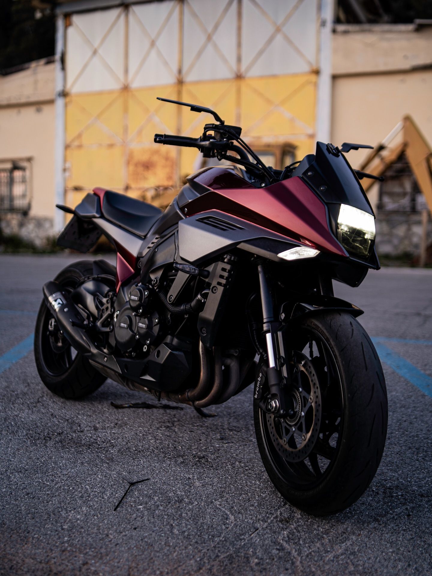 Una motocicletta sportiva nera e magenta parcheggiata sull'asfalto davanti a un magazzino al crepuscolo.
