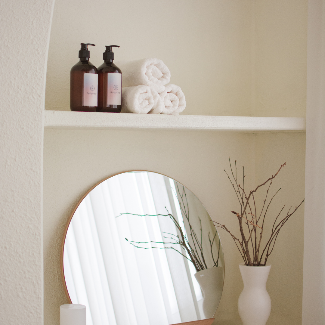 Two bottles of lotion sit on a shelf above a round mirror