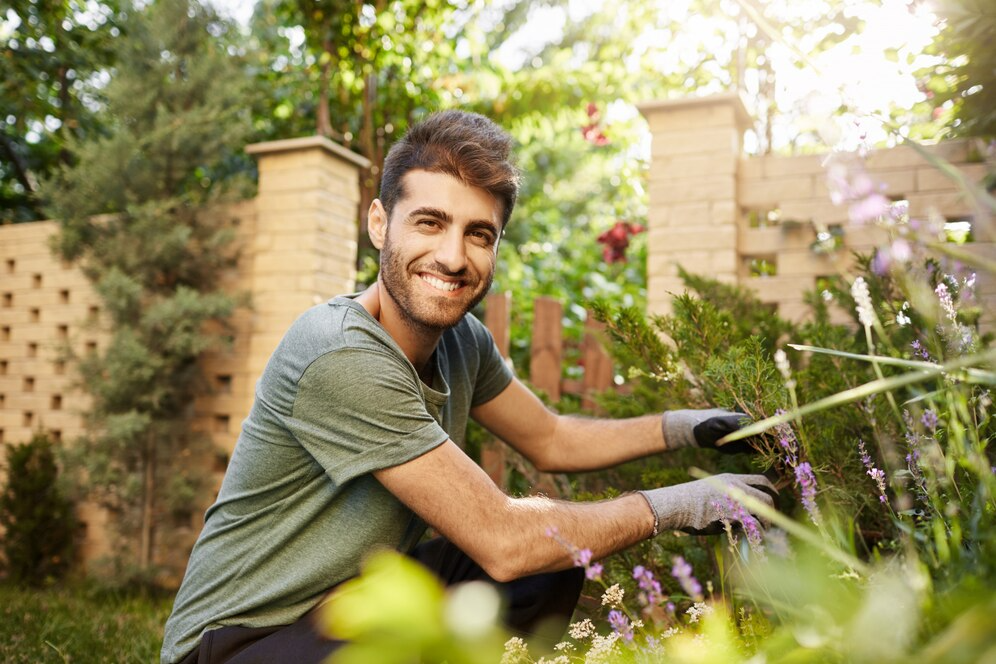 A man is kneeling down in a garden cutting flowers.