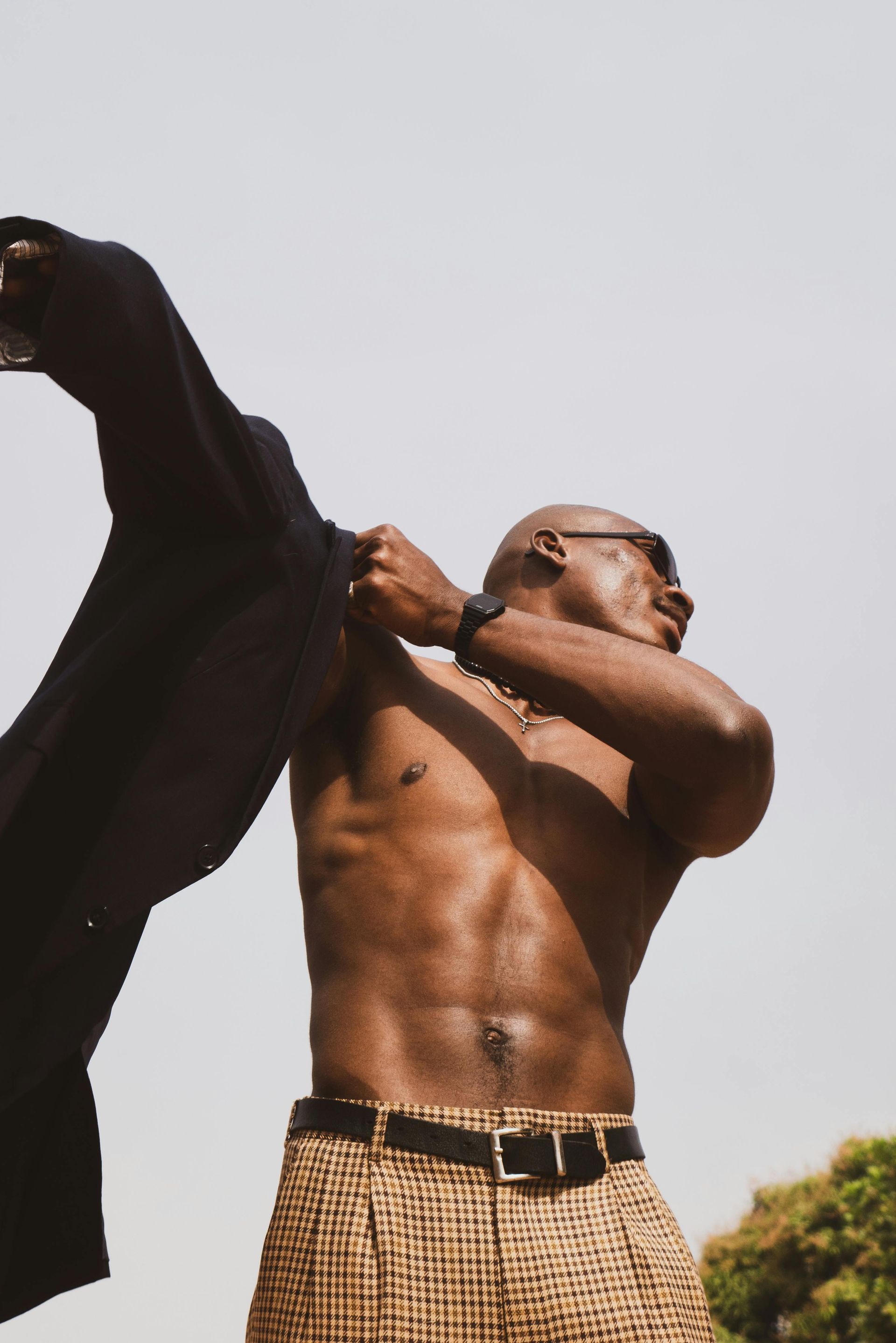 A shirtless man is taking off his jacket.