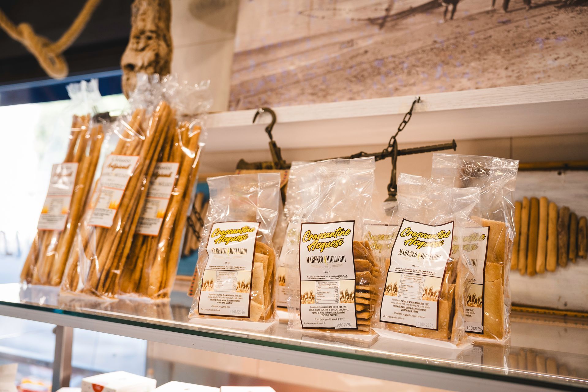 Snack confezionati esposti su uno scaffale di vetro in un negozio, con etichette beige e bianche.