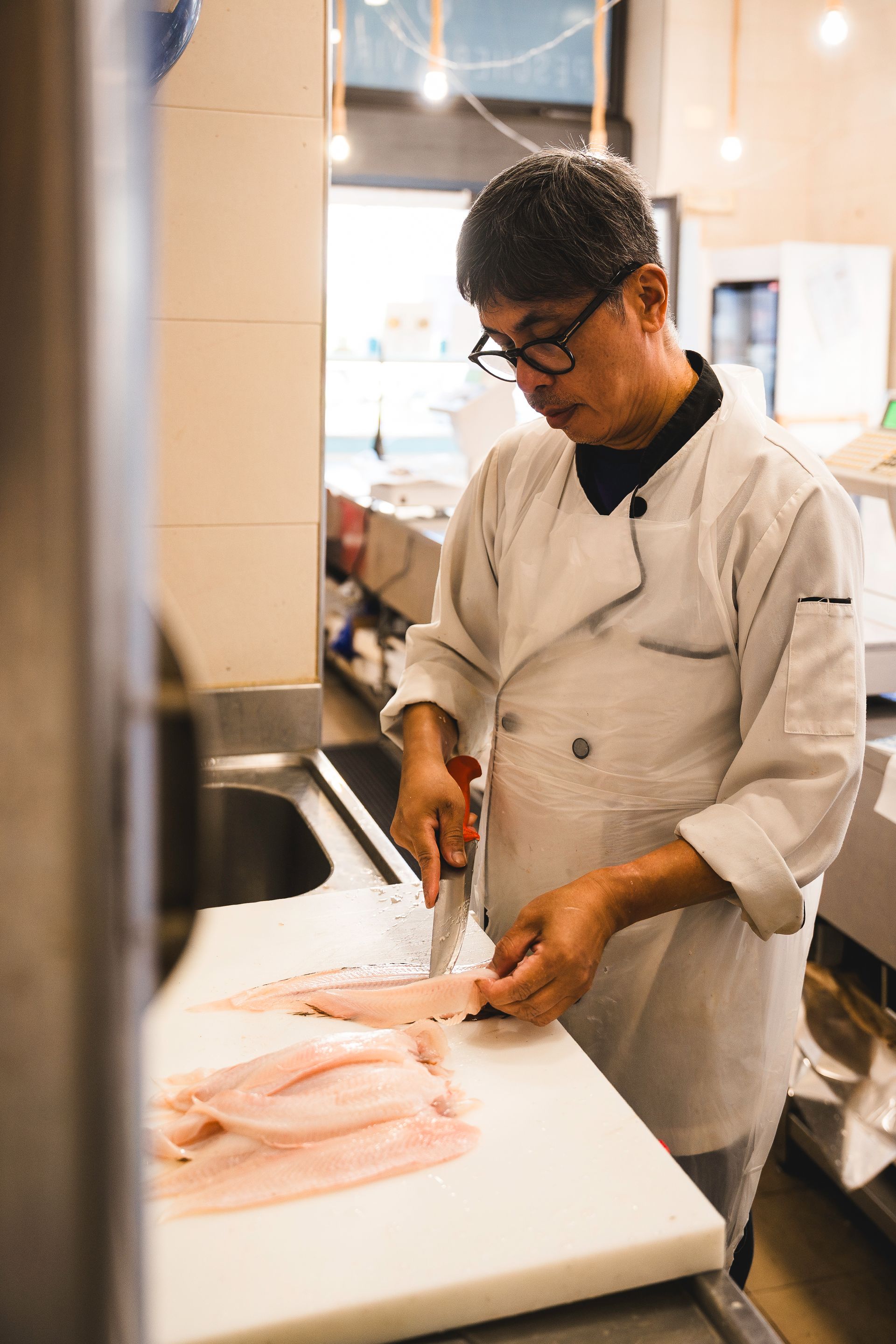 In una cucina luminosa, lo chef affetta filetti di pesce rosa su un tagliere.