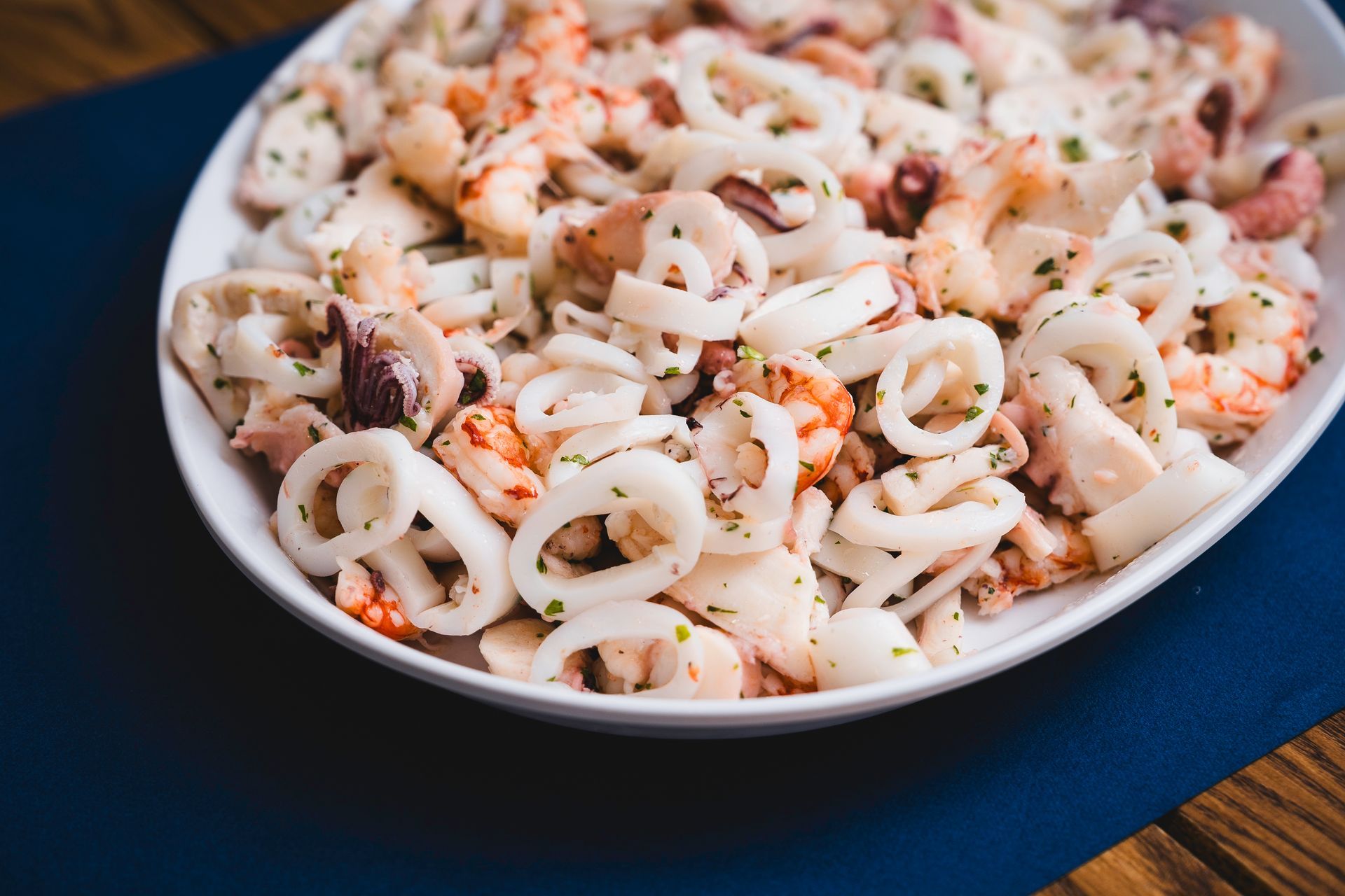 Piatto di insalata di mare con anelli di calamari ed erbe aromatiche tritate su una tovaglia blu.