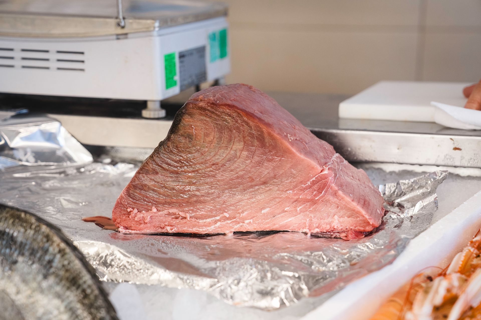 Un grosso pezzo di carne cruda su un bancone ricoperto di carta stagnola, accanto a una bilancia da cucina.