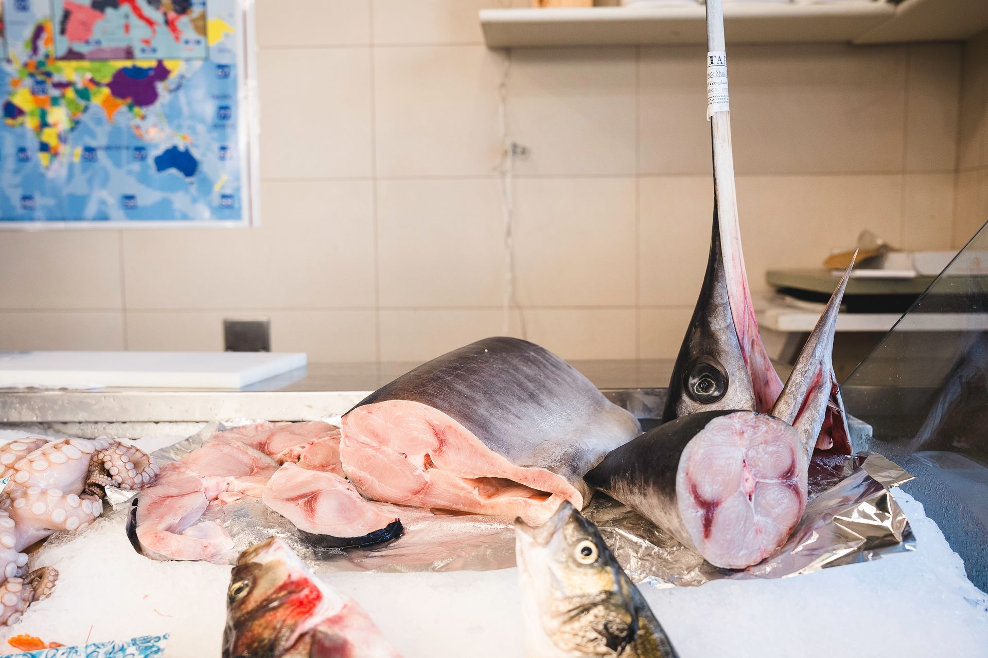 Pesce fresco esposto su un bancone del mercato, con scaffali e opere d'arte alle pareti sullo sfondo.