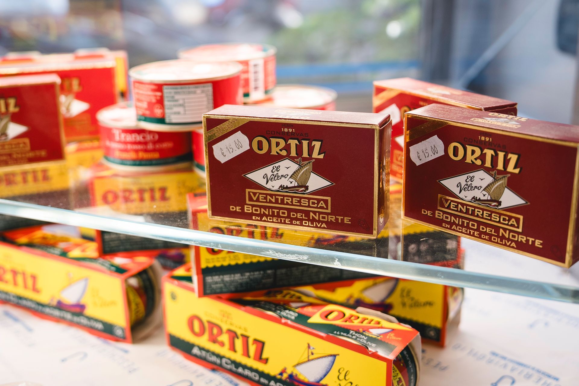 Scatole di pesce in scatola Ortiz di vario tipo impilate sugli scaffali del negozio, protette da una teca di vetro.