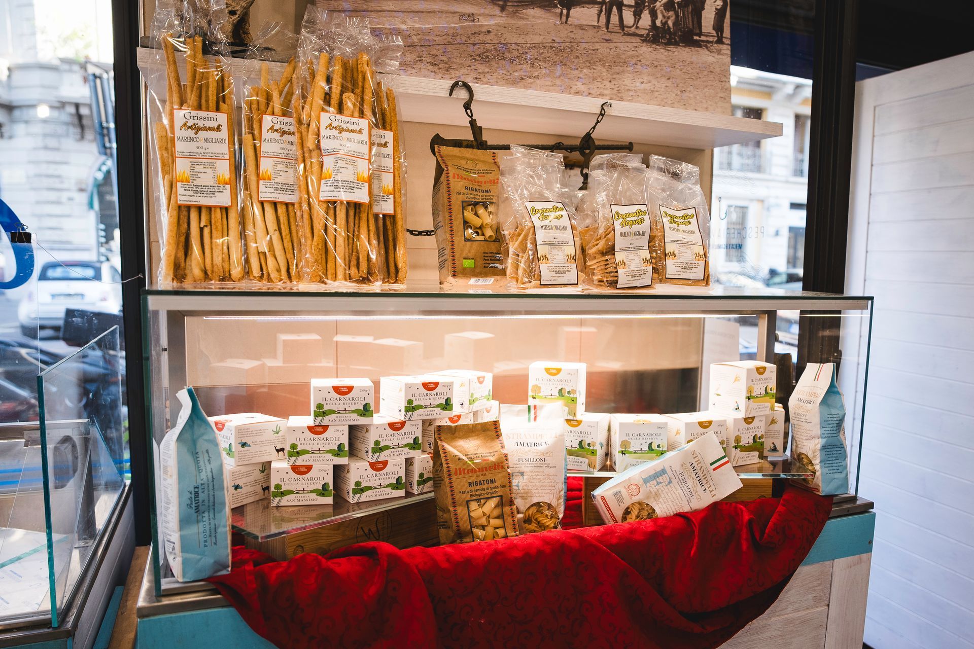 Un'ampia esposizione di snack confezionati e vasetti su scaffali di vetro, con un drappo rosso sottostante.