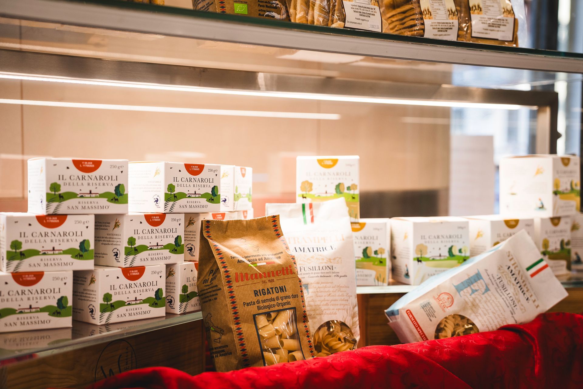Snack confezionati assortiti esposti dietro un vetro in una vetrina da panetteria, con un telo rosso davanti.