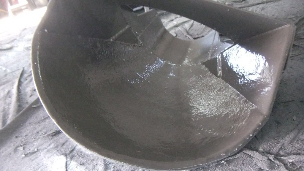 Conteneur incurvé en métal gris foncé, probablement de fabrication industrielle, détail intérieur avec surface brillante et humide.