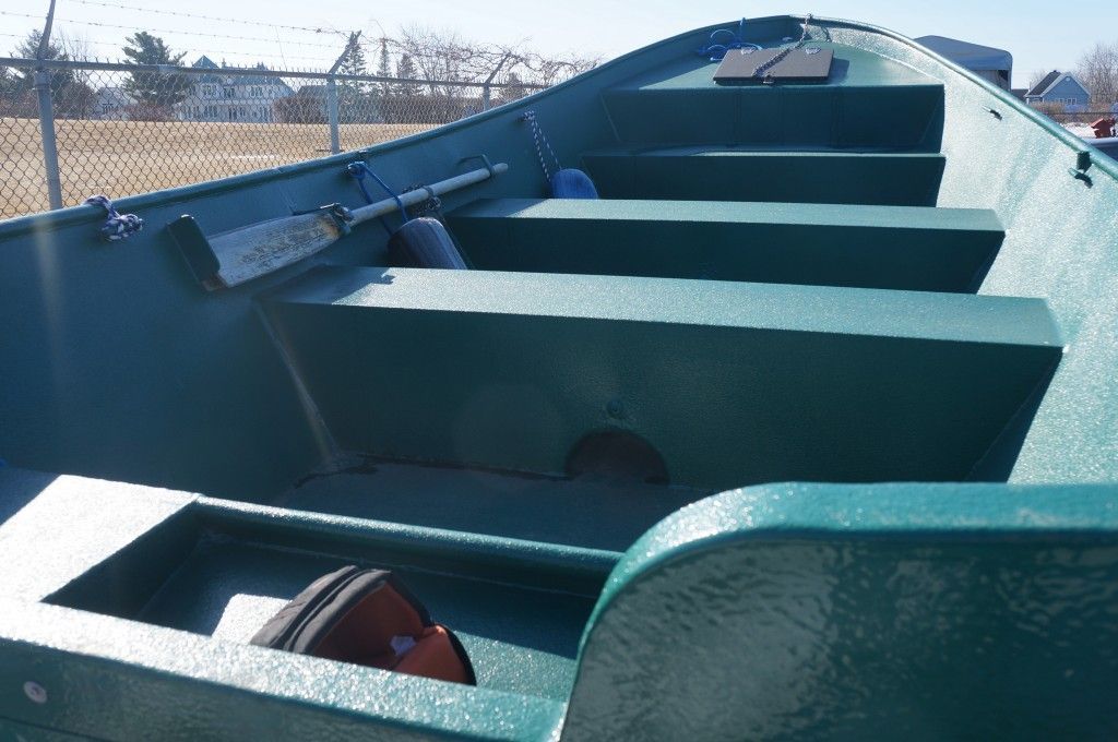 Intérieur du bateau vert avec banquettes et rames.
