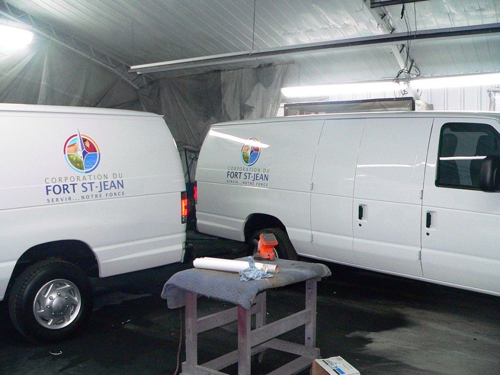 Deux camionnettes blanches avec des logos dans un garage, du matériel sur une petite table.