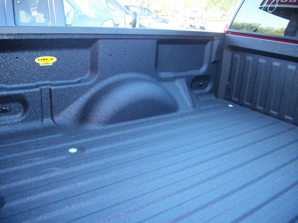 Plateau de pick-up noir avec revêtement texturé. Comprend un passage de roue, des anneaux d'arrimage et un panneau latéral.