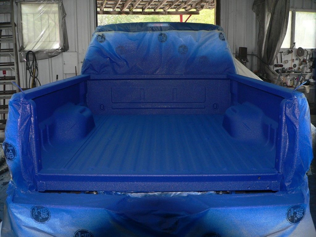 Benne de camion peinte en bleu, recouverte d'une bâche de protection bleue. Vue de l'arrière, à l'intérieur d'un atelier.