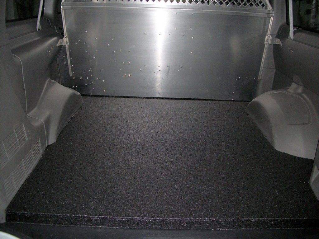 Espace de chargement d'une camionnette, avec un tapis de sol noir texturé et des panneaux métalliques.