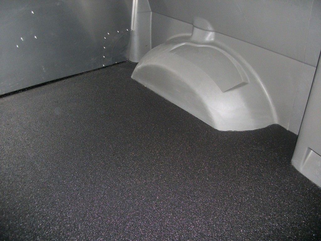 Un revêtement de sol texturé noir a été installé dans l'espace de chargement gris clair d'un véhicule, recouvrant le sol.