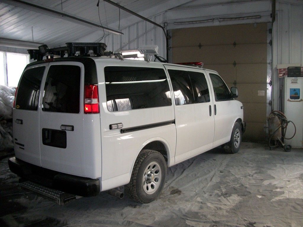 Fourgonnette blanche avec équipement sur le toit et une rampe, garée dans un garage.