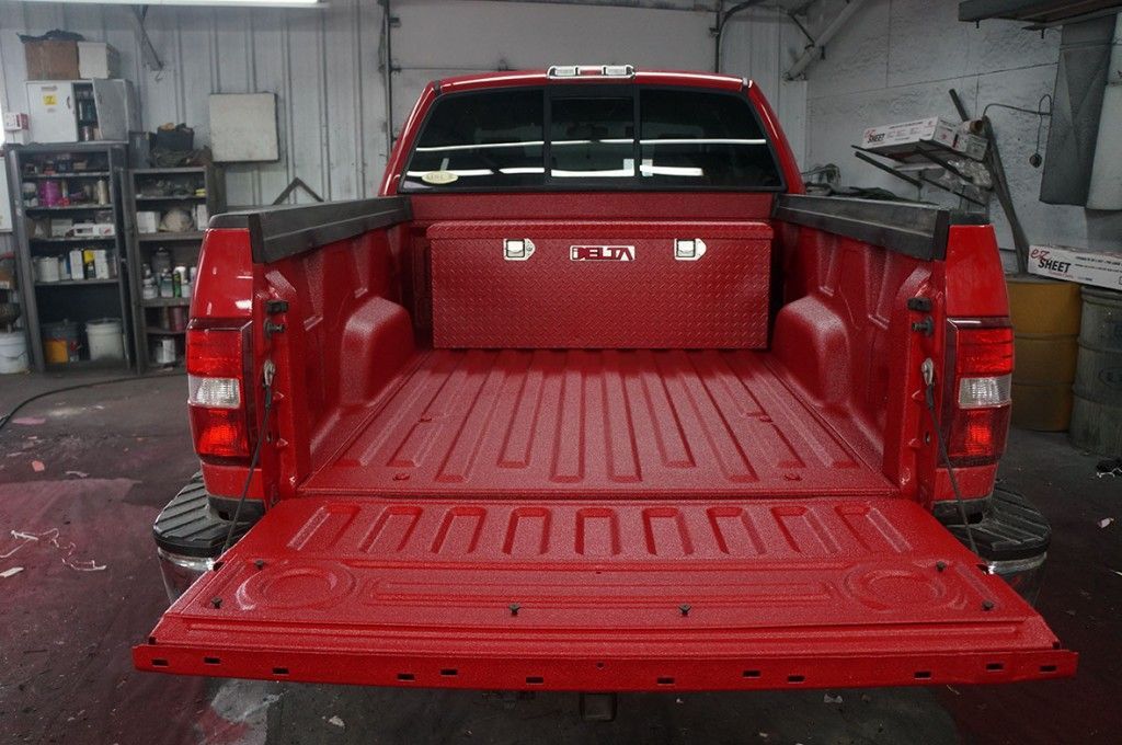 Plateau de pick-up rouge avec hayon ouvert et coffre à outils en tôle larmée.