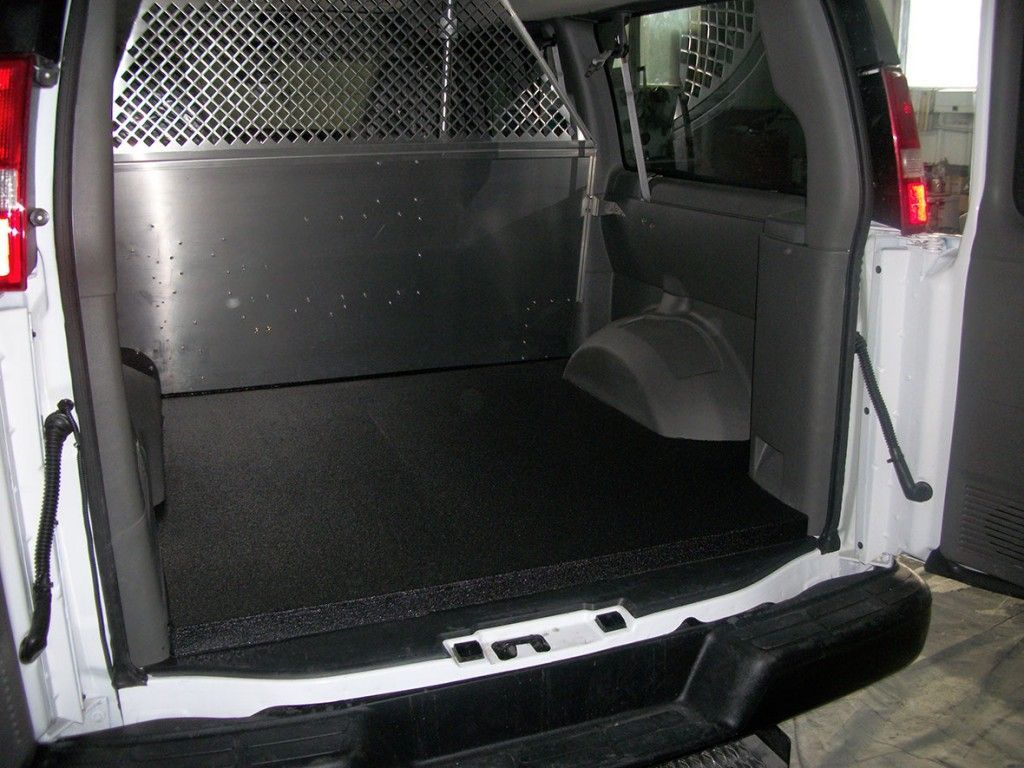 Intérieur d'une camionnette blanche avec un plancher noir et une cloison de séparation métallique pour le chargement.
