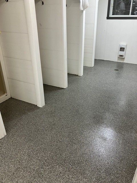 Salle de bains avec sol gris moucheté, cabines blanches et une petite fenêtre.