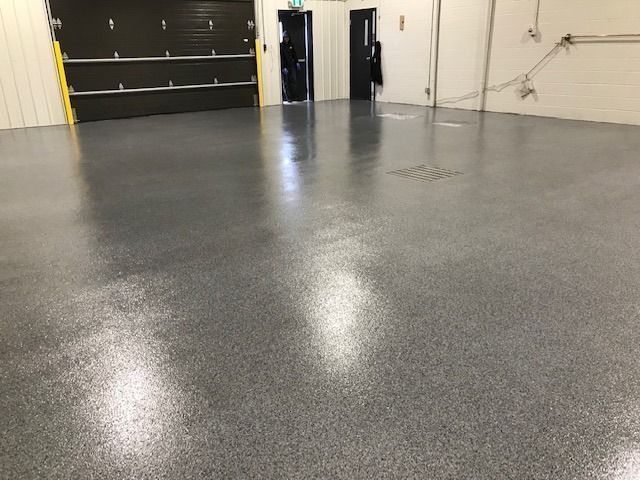 Un grand espace industriel vide, avec un sol en époxy gris brillant et moucheté.