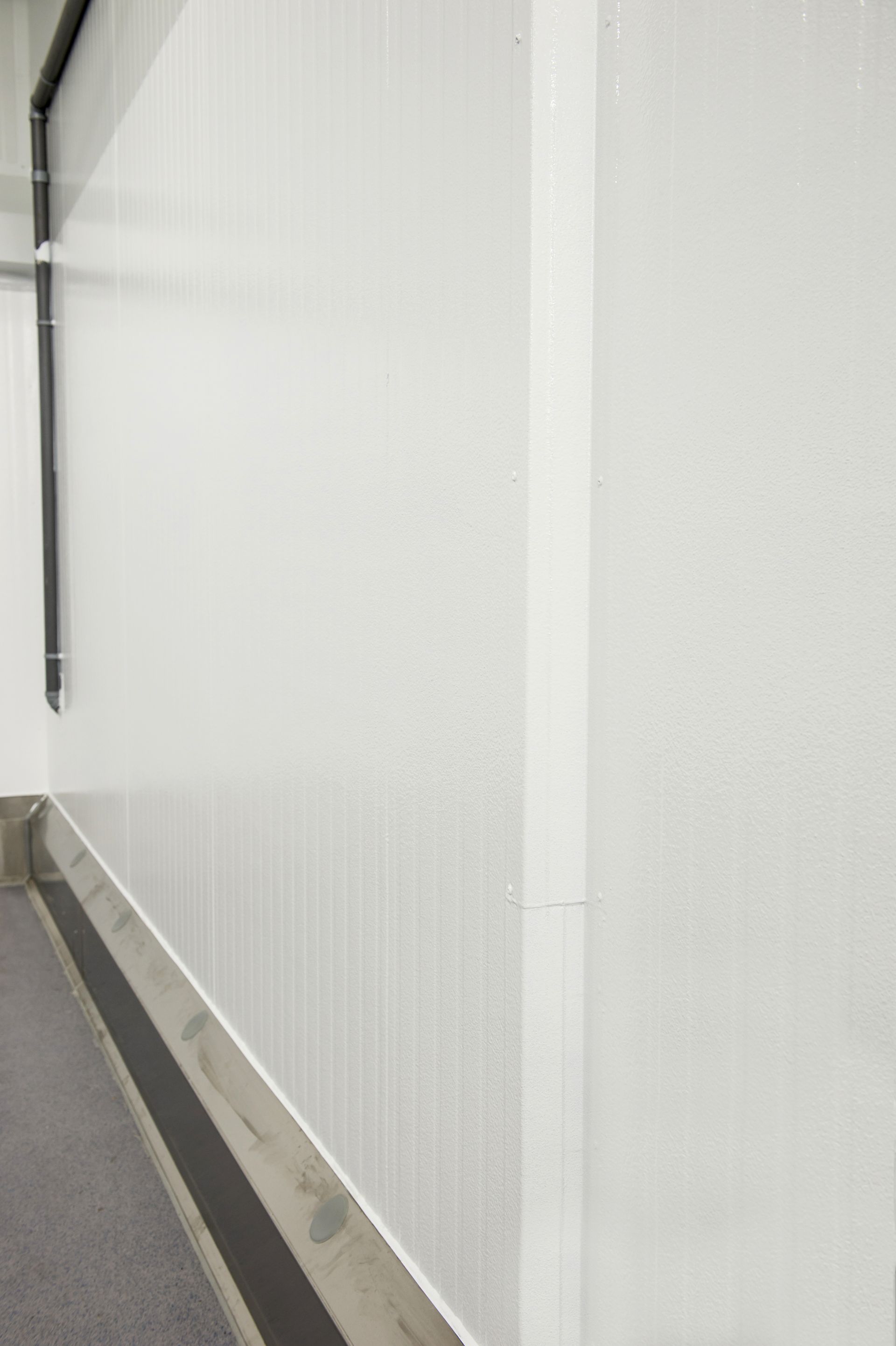 Intérieur blanc avec un tuyau noir au mur et un sol gris avec une bande foncée.