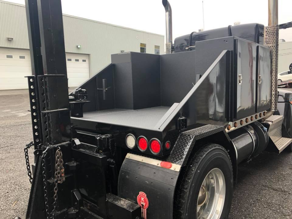 Arrière d'un camion de dépannage noir avec plateau, espace de rangement et feux arrière.