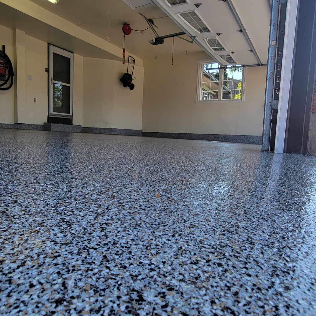 Un garage avec un sol en époxy gris moucheté, une porte de garage fermée à droite et une porte à gauche.