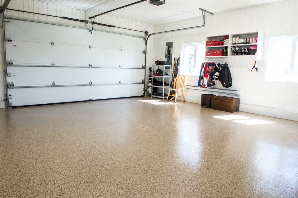 Garage vide avec un sol en époxy moucheté, une porte de garage blanche fermée et des étagères.
