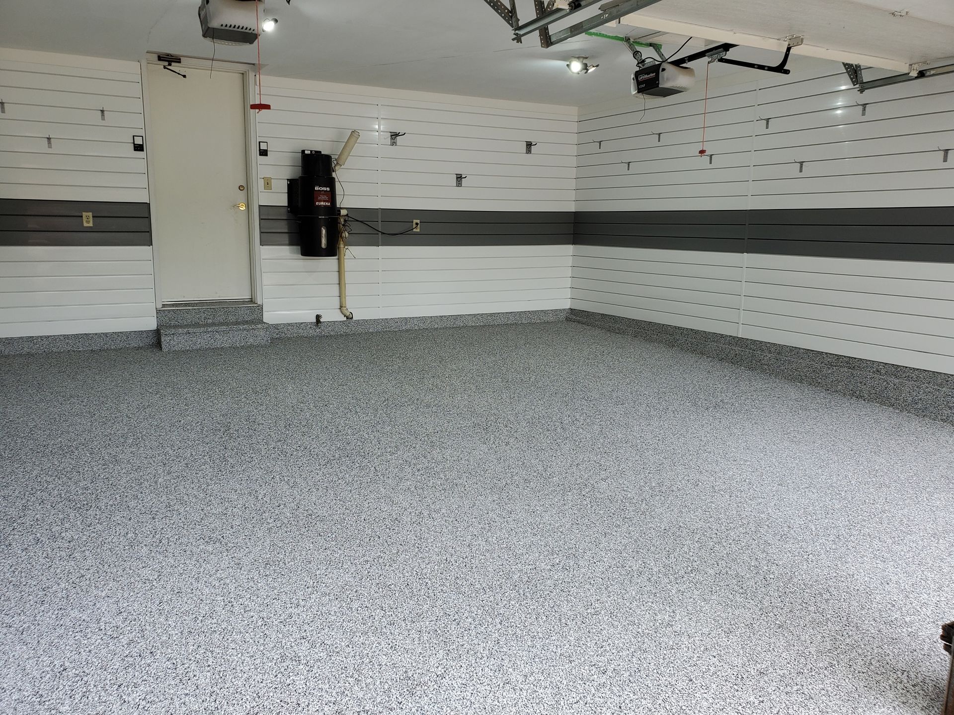 Intérieur de garage avec sol en époxy, murs blancs et gris et porte fermée.