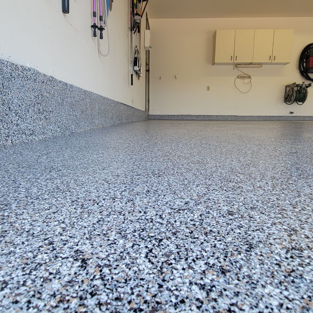 Garage avec un sol en époxy moucheté. On aperçoit les murs blancs, les outils et les armoires.