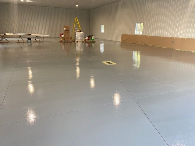Sol spacieux en époxy gris clair dans un grand bâtiment industriel vide. Surface réfléchissante, couleurs neutres.