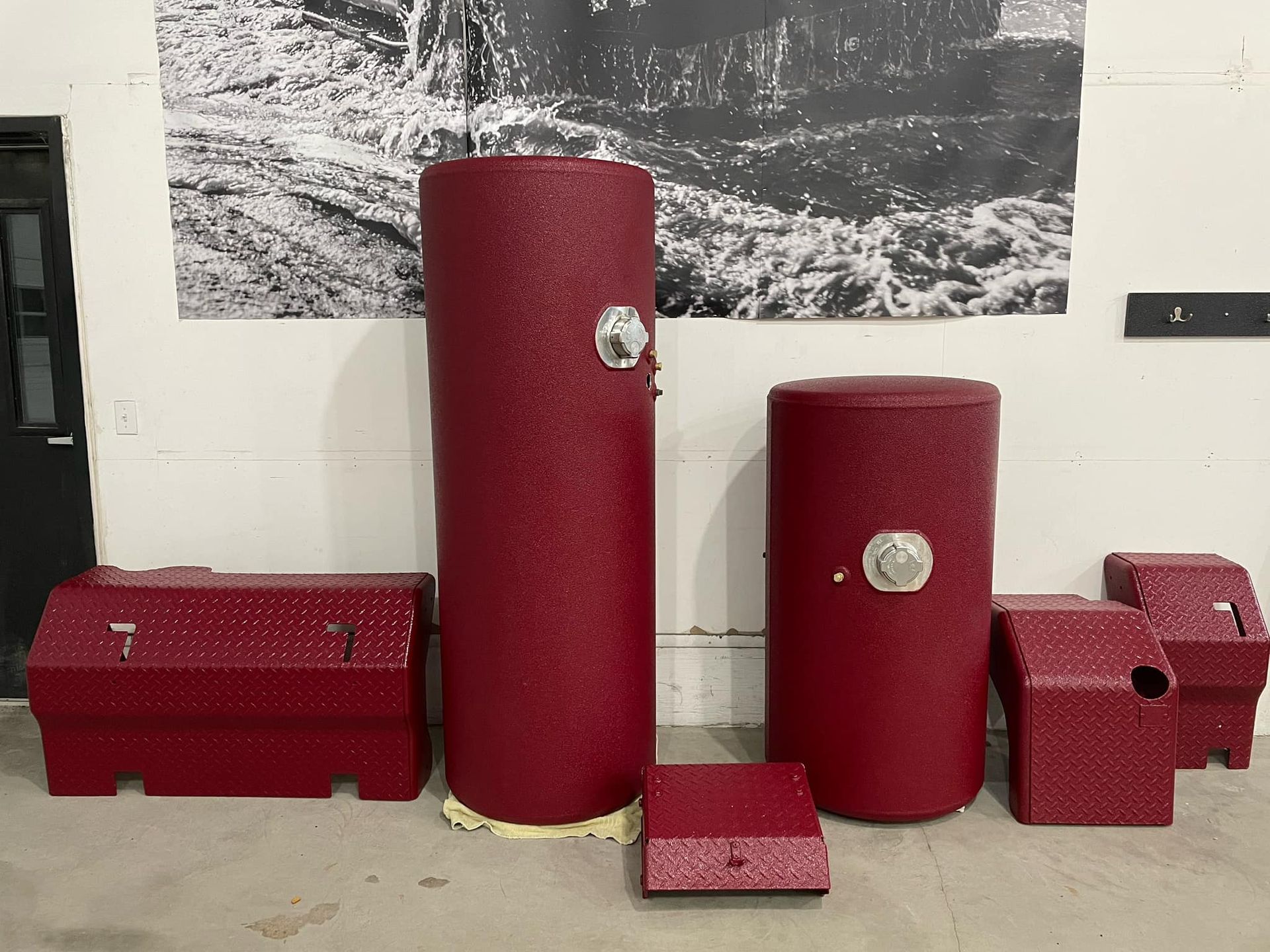 Plusieurs conteneurs de rangement rouges, cylindriques et rectangulaires, sont disposés dans une pièce, avec une photo en noir et blanc en arrière-plan.