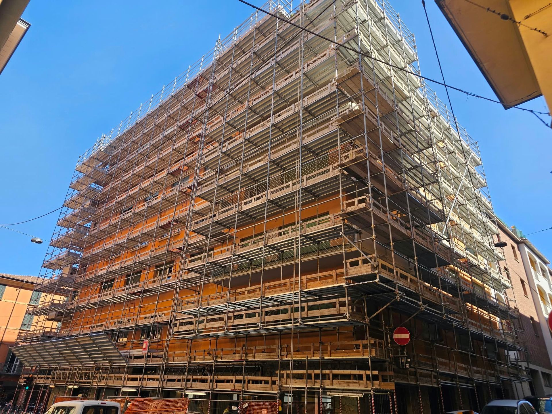 Scaffolding wrapped around a multi-story building under construction against a blue sky