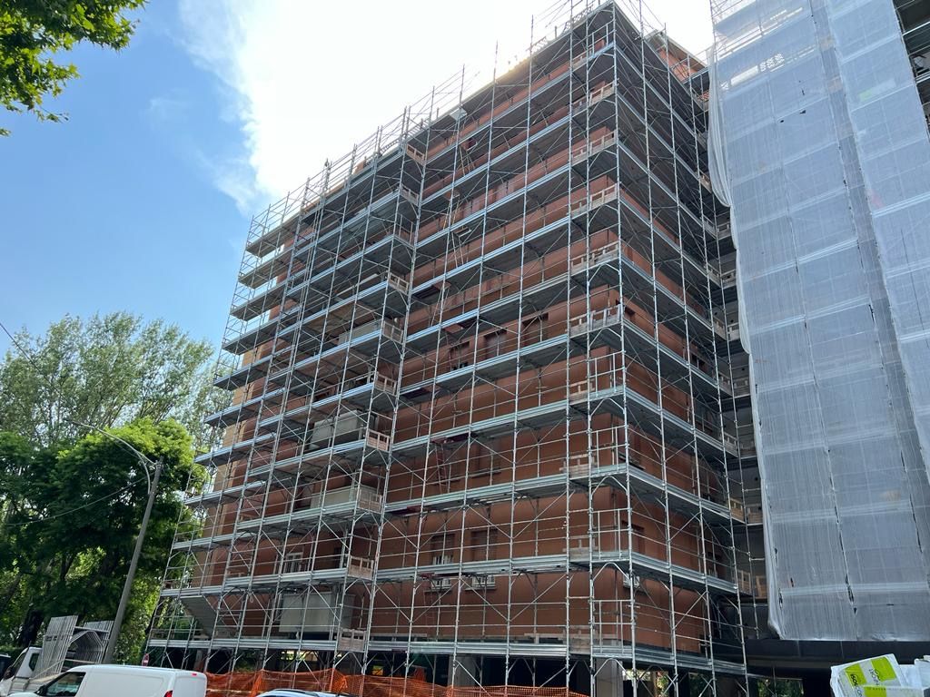 Red brick building under construction beside a glass high-rise, covered in scaffolding.