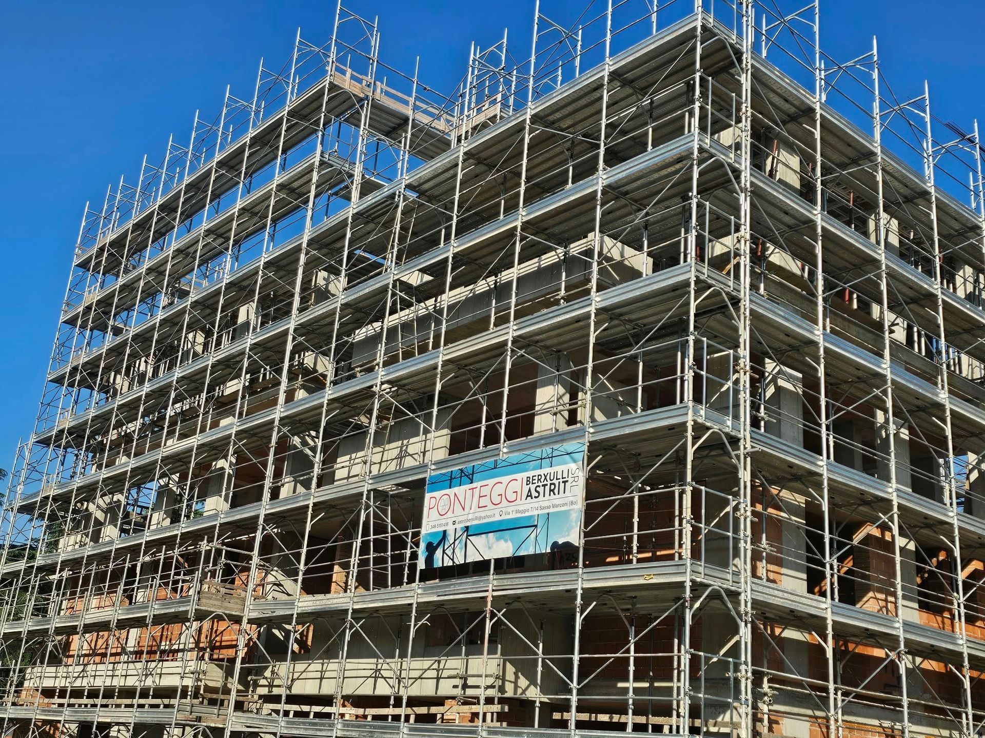 Scaffolding surrounds a multi-story building under construction against a blue sky