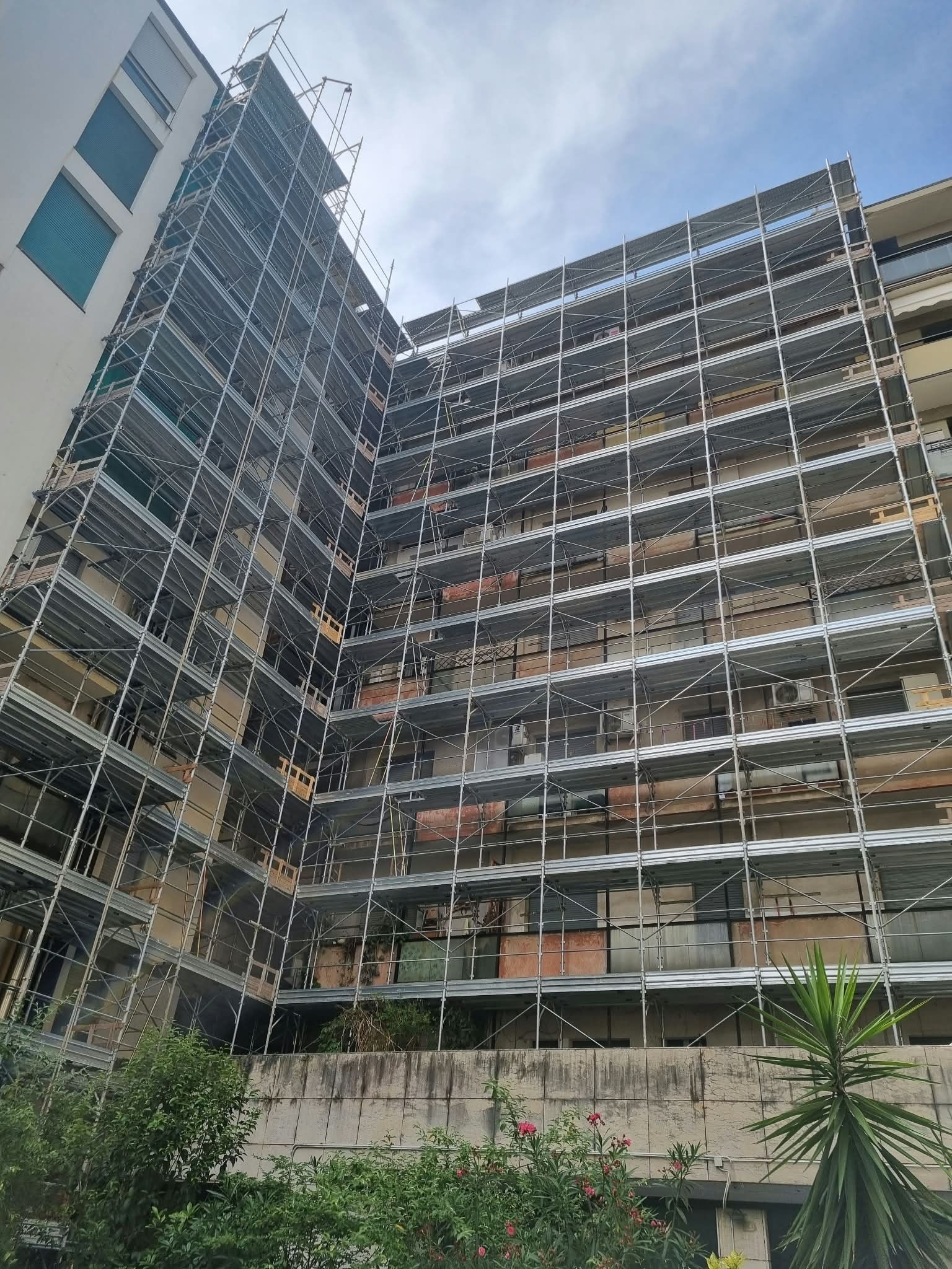 Multi-story building under construction with scaffolding and exposed floors against a blue sky