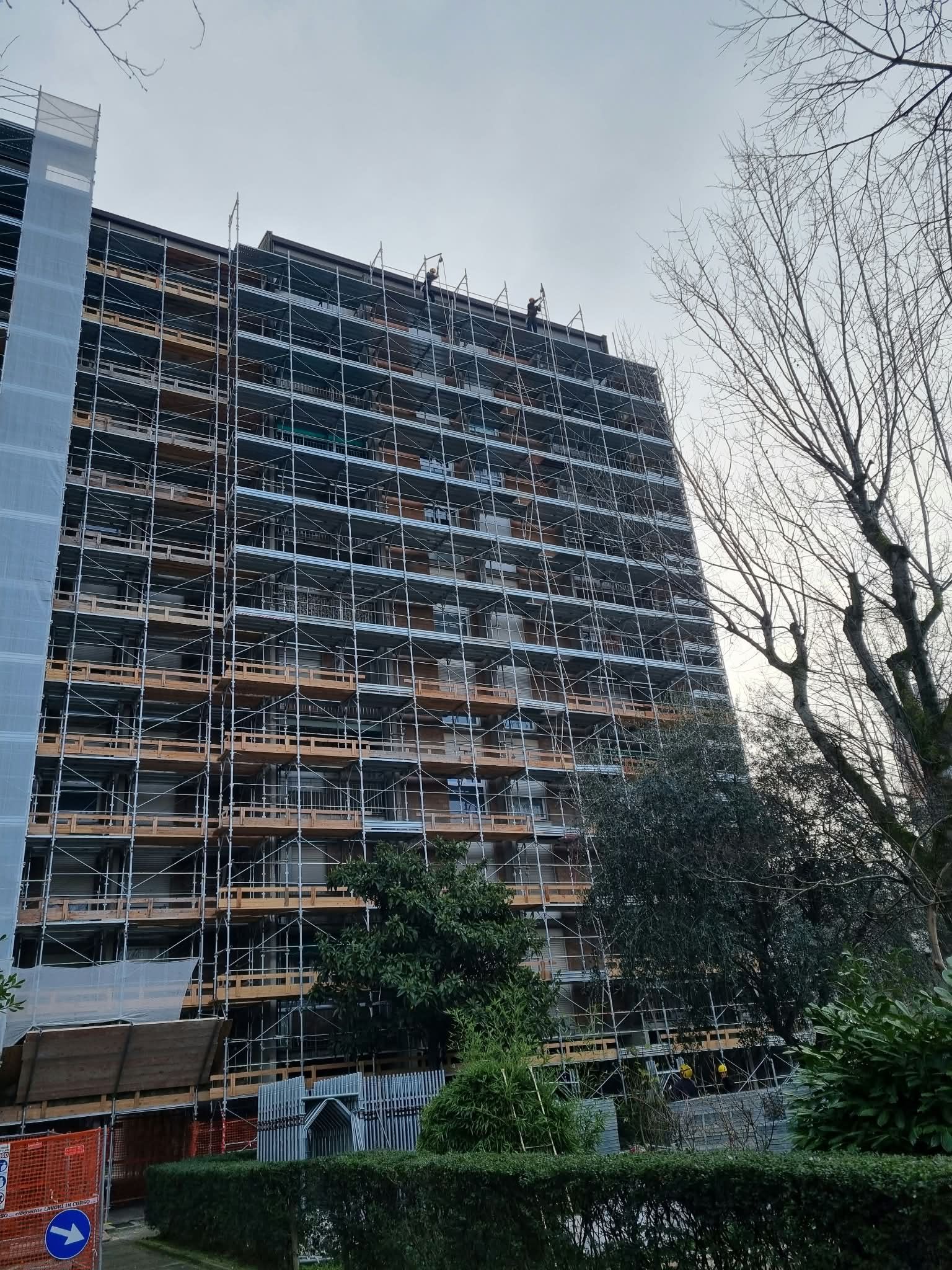 Tall apartment building under construction beside bare trees and greenery at dusk