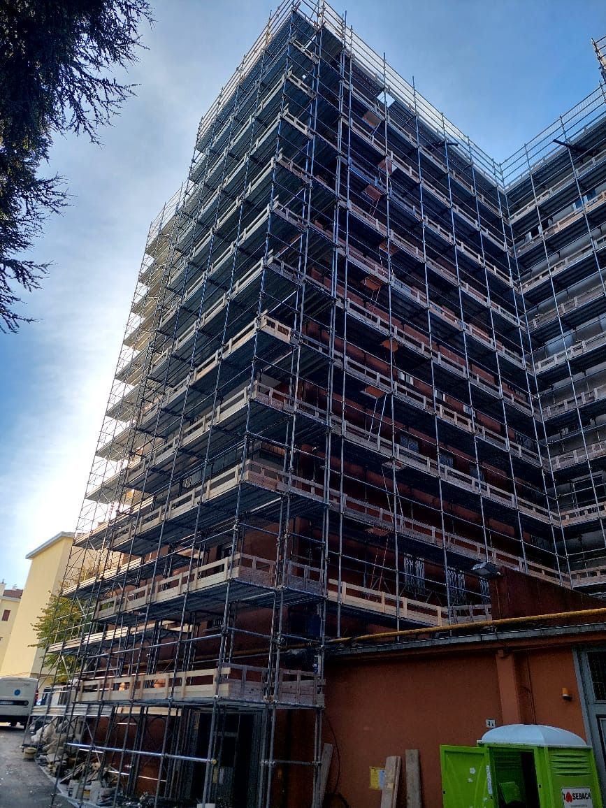Scaffolded high-rise building under construction beside a smaller building on a cloudy day