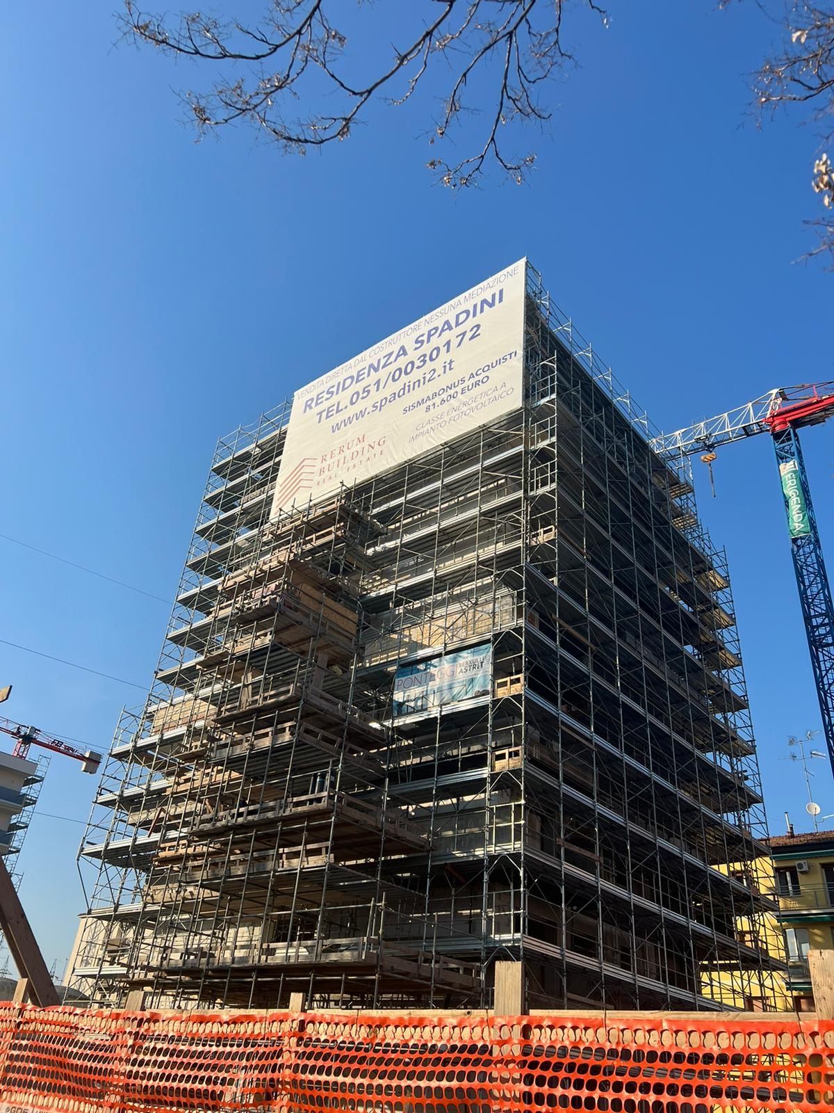 Multi-story building under construction, wrapped in scaffolding against a clear blue sky.