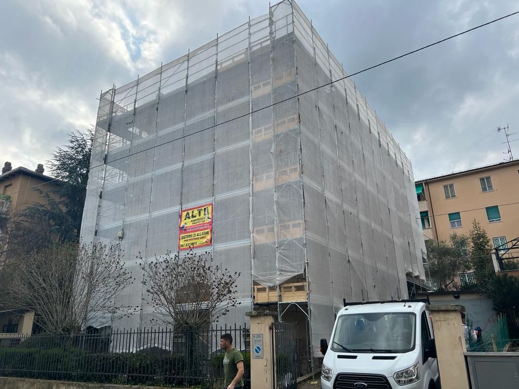 Building wrapped in white construction netting, with a white van parked in front under a cloudy sky.