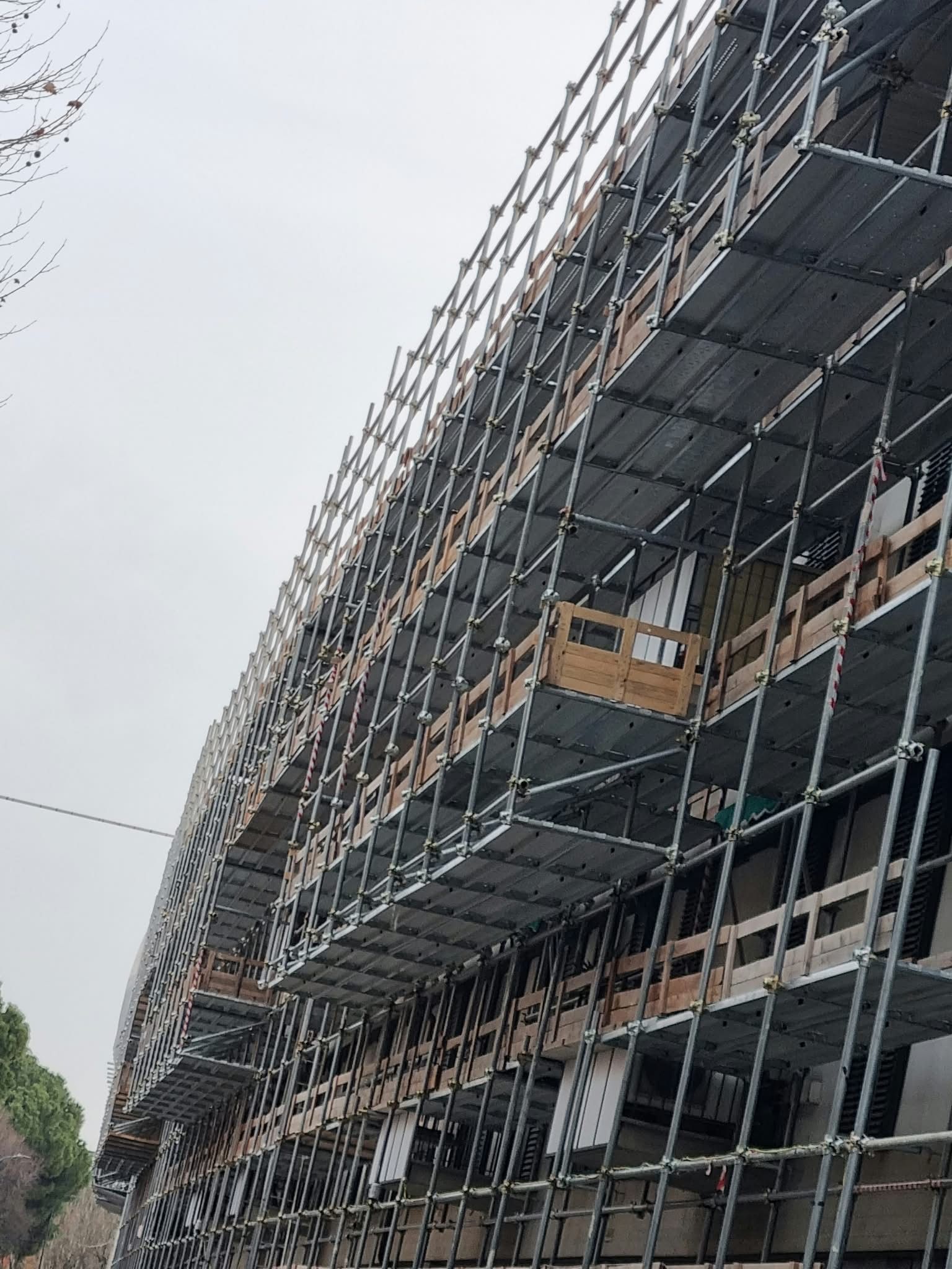 Curved building under construction with scaffolding and exposed glass facade under an overcast sky