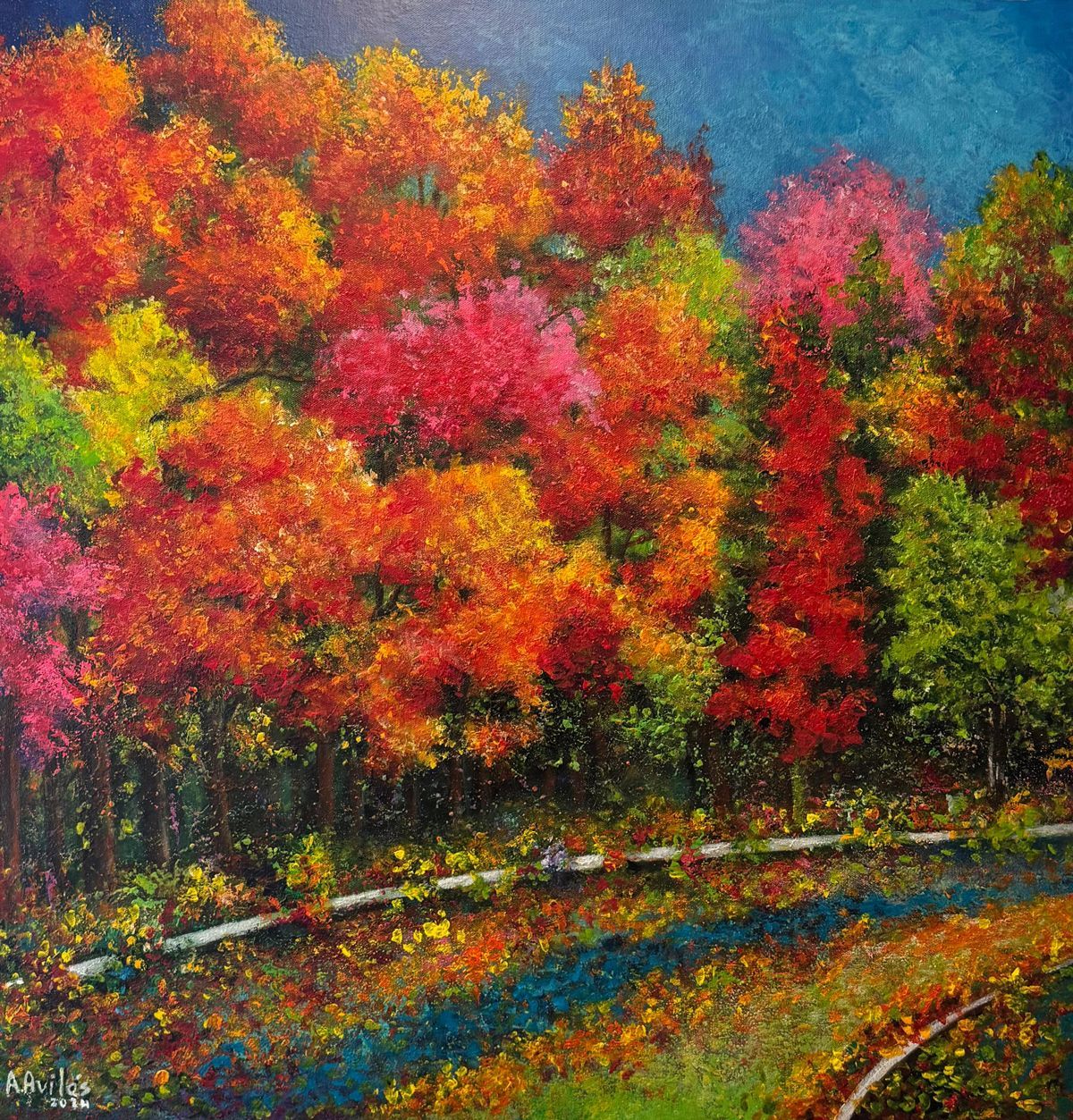 Autumn trees in vivid red, orange, and yellow beside a curving path under a blue sky