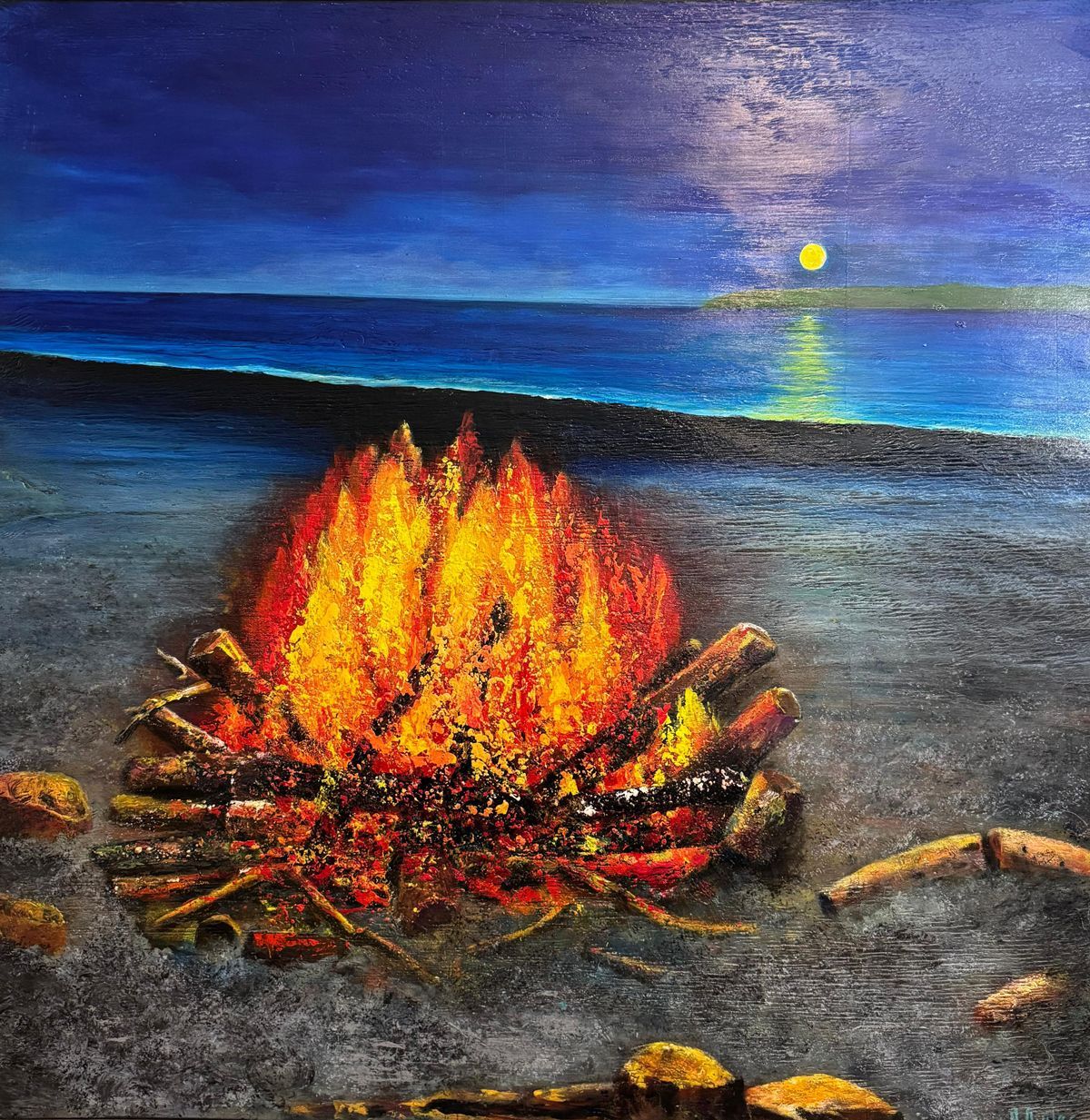 Bonfire burning on a dark beach at dusk, with the moon over the ocean and blue sky.