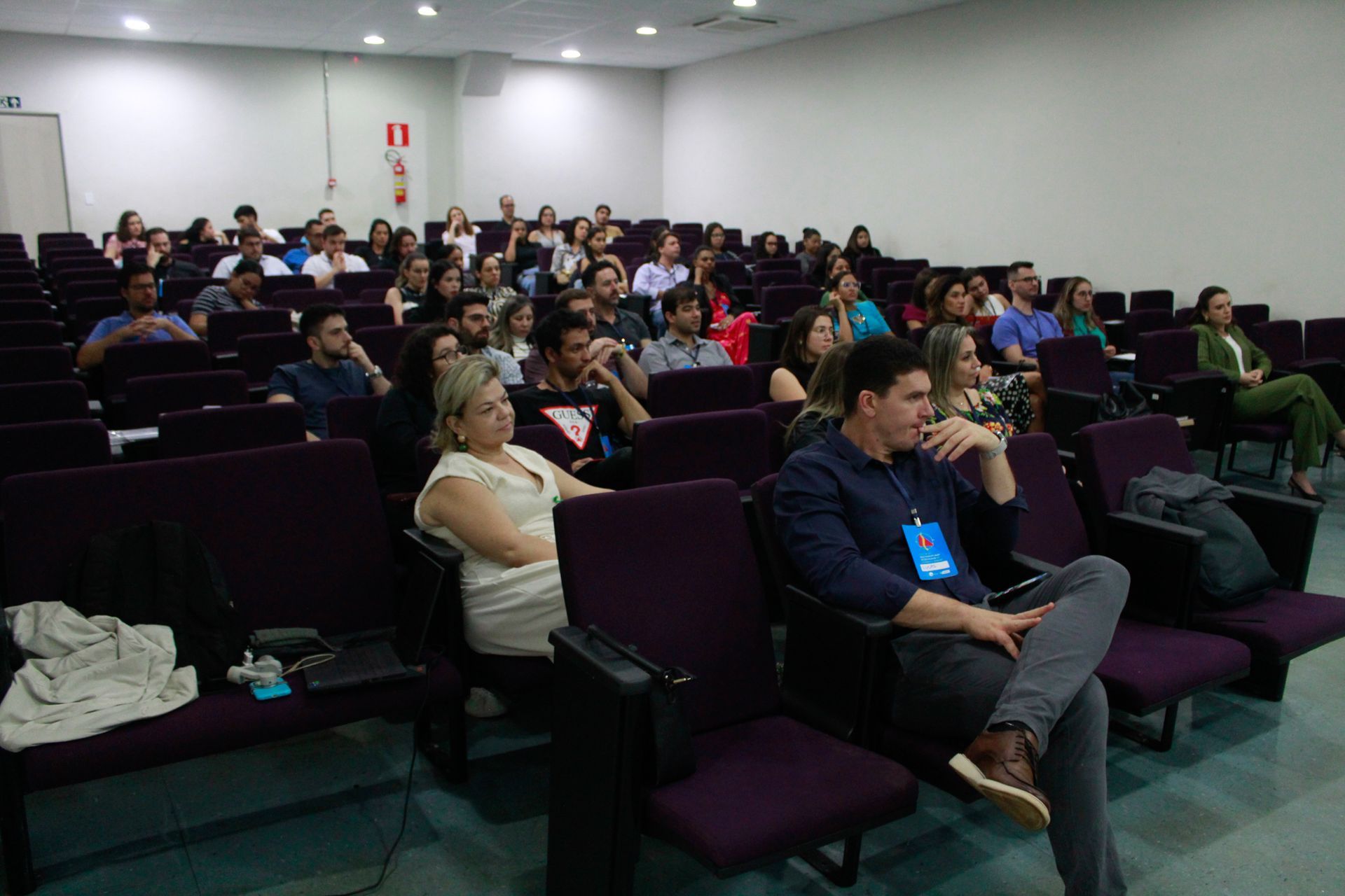 Um grupo de pessoas está sentado em cadeiras roxas em um auditório.