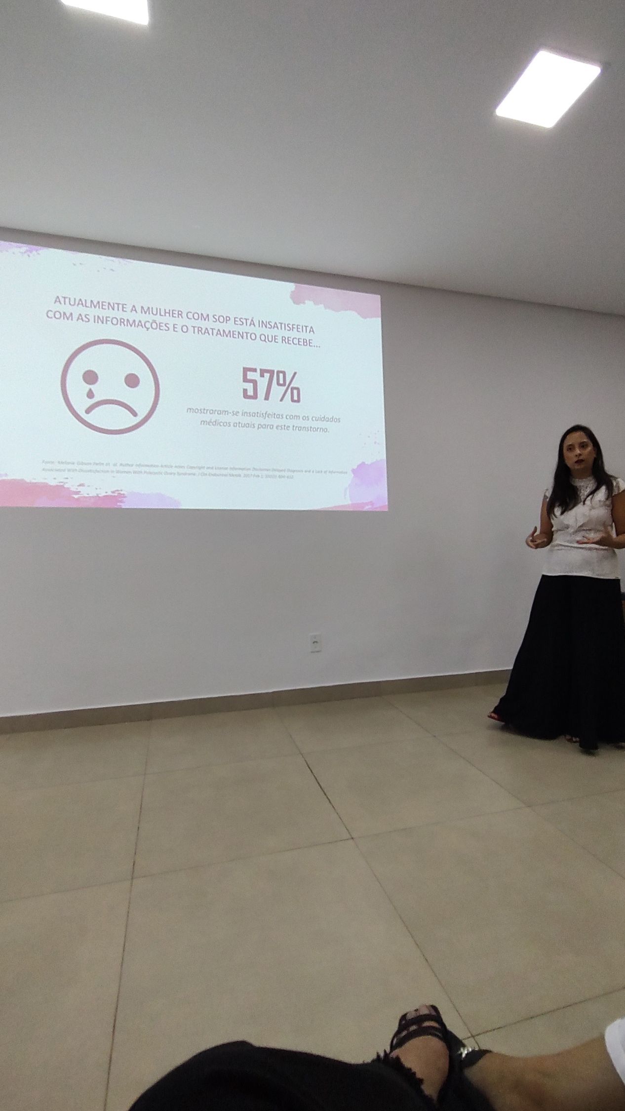 Dra Francine fazendo uma apresentação em frente a uma tela de projetor.