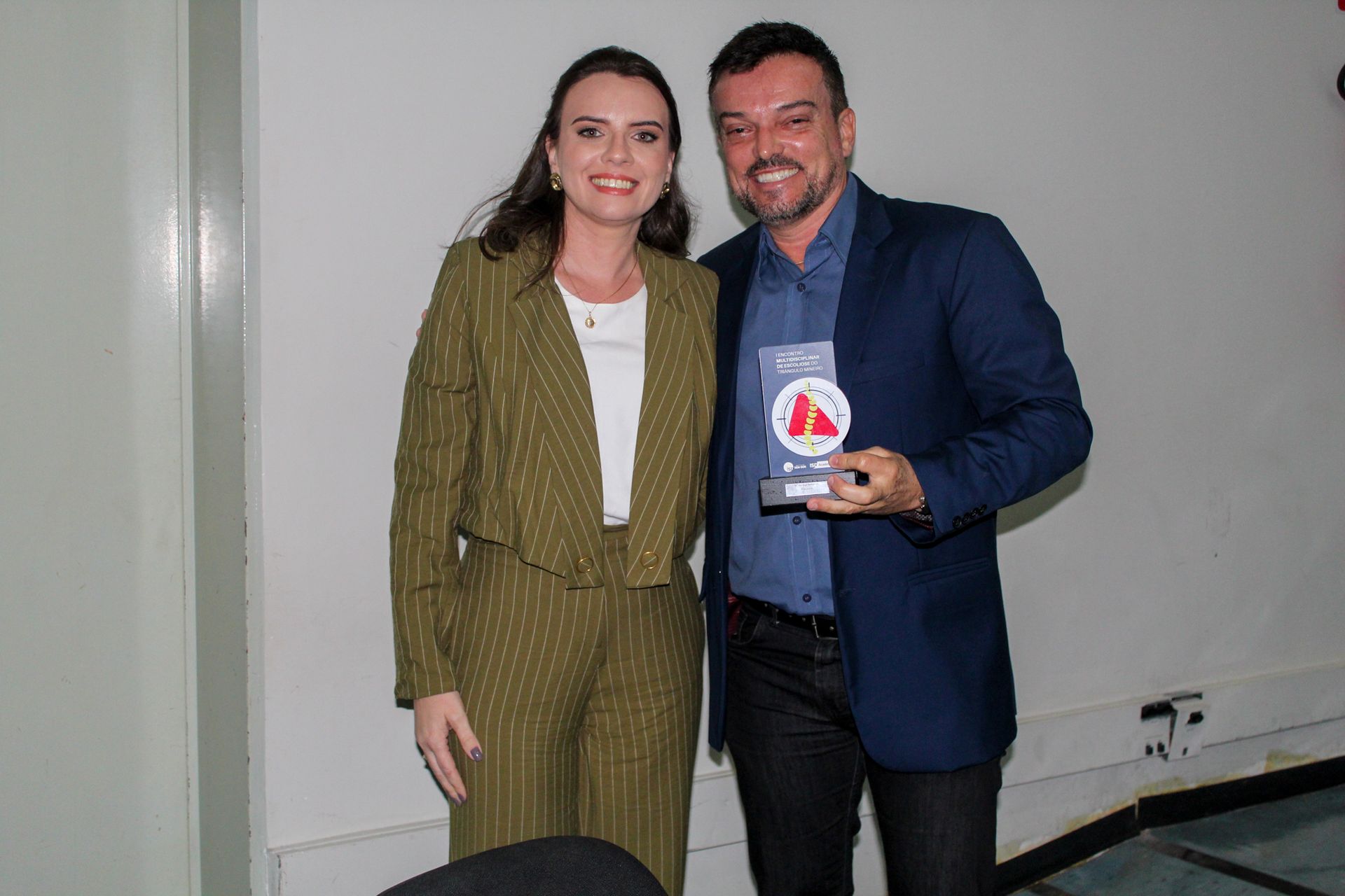 Um homem e uma mulher estão de pé, um ao lado do outro, segurando um troféu.